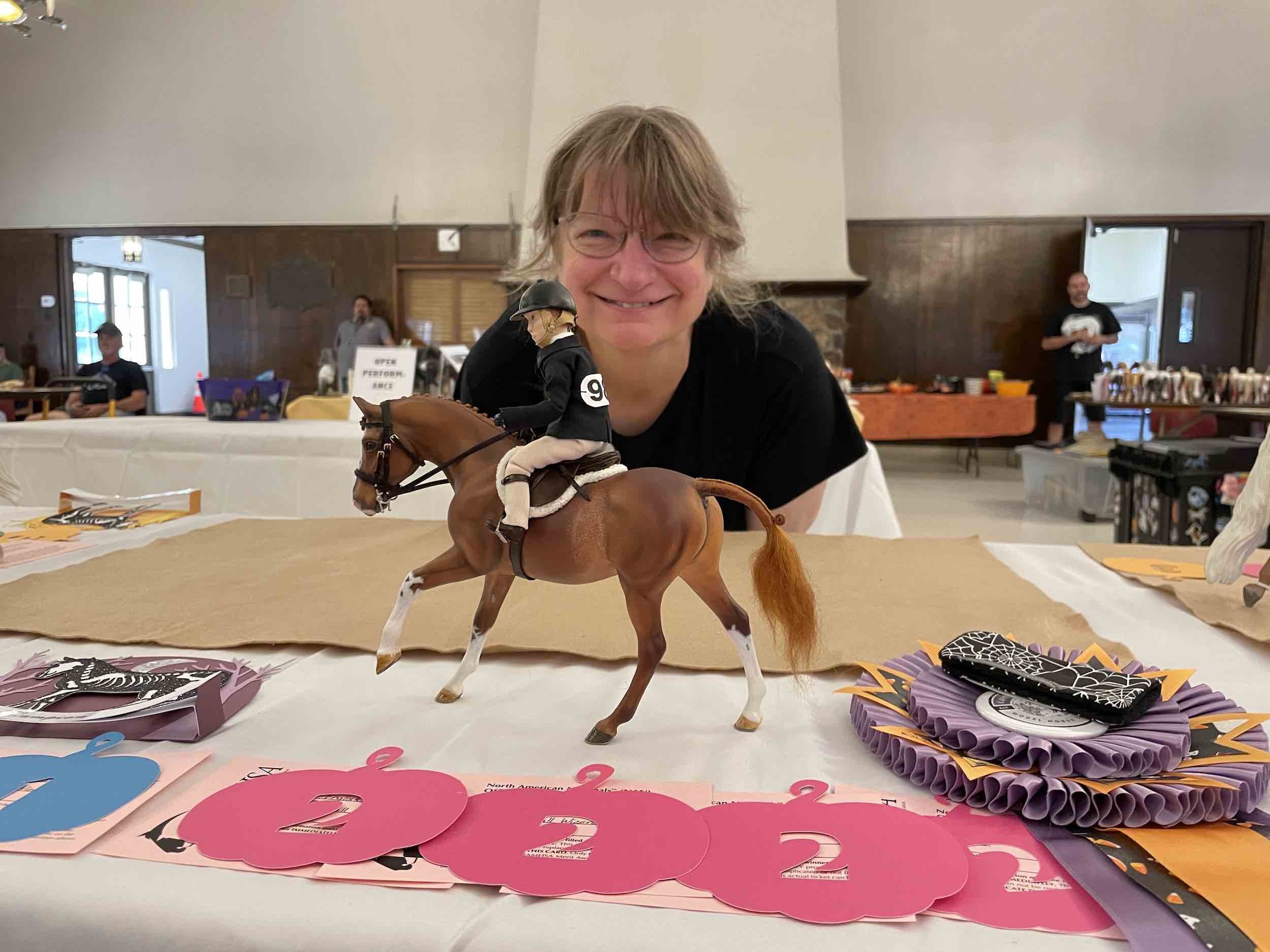 A chestnut pony with awards including rosettes with the owner behind
